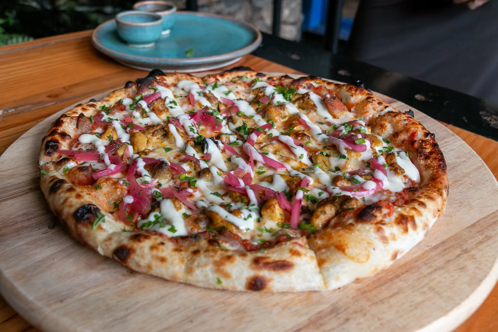 Pizza D'Eli: pollo marinado, alioli y cebolla morada, sobre tabla de madera