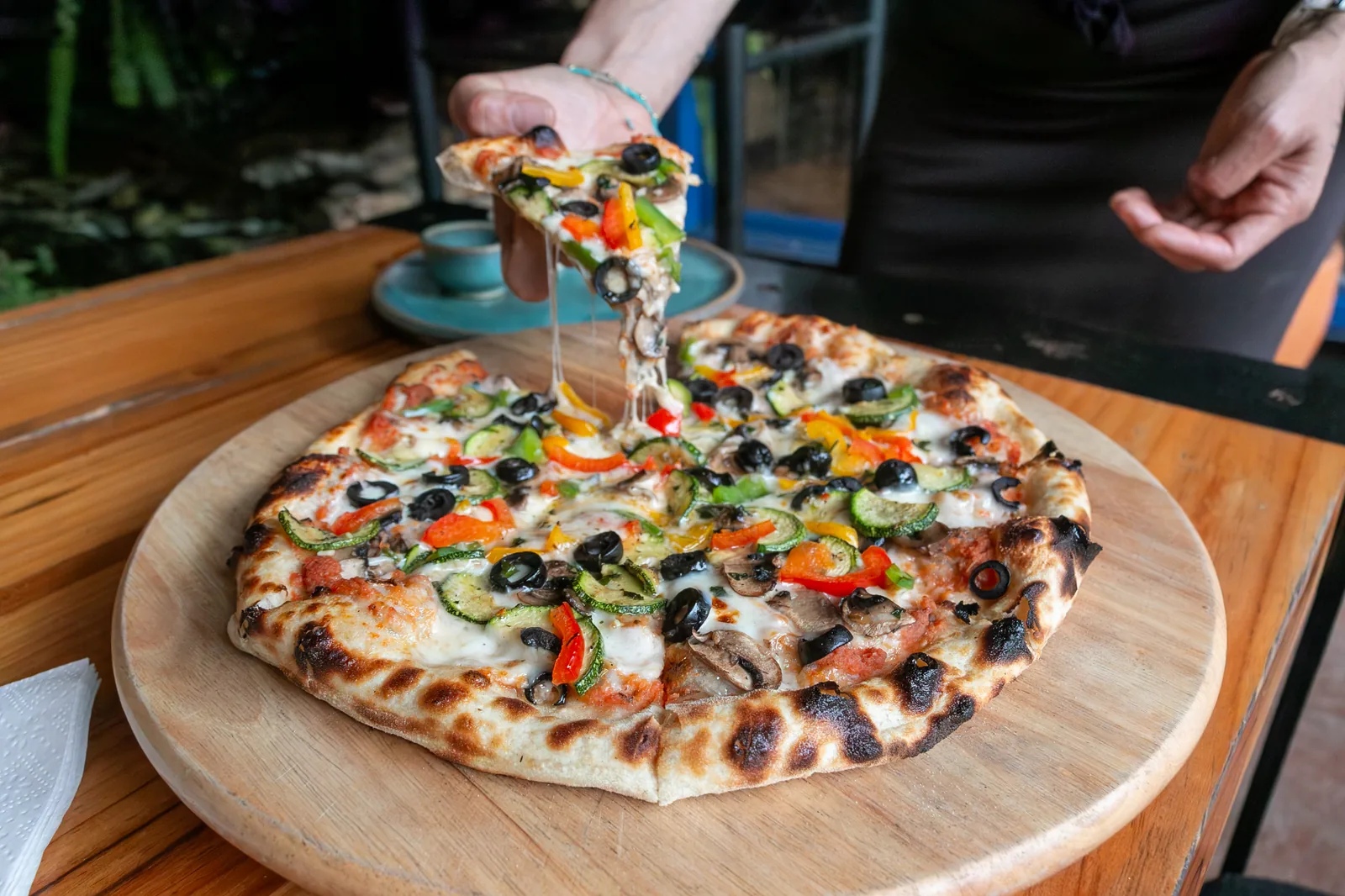 Pizza vegetariana con champiñón, aceituna, calabacita y pimientos, con una rebanada levantándose